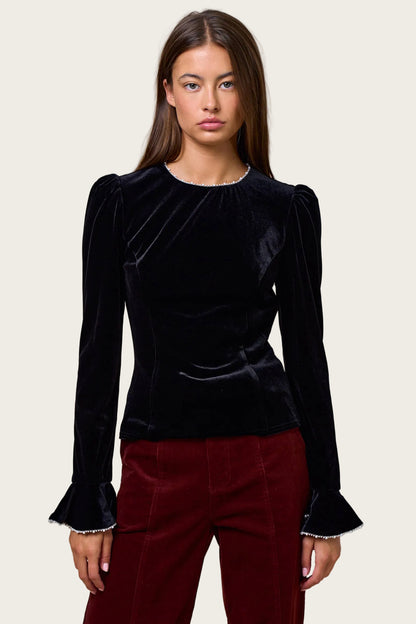 Woman wearing a black velvet top with long sleeves and red pants on a beige background