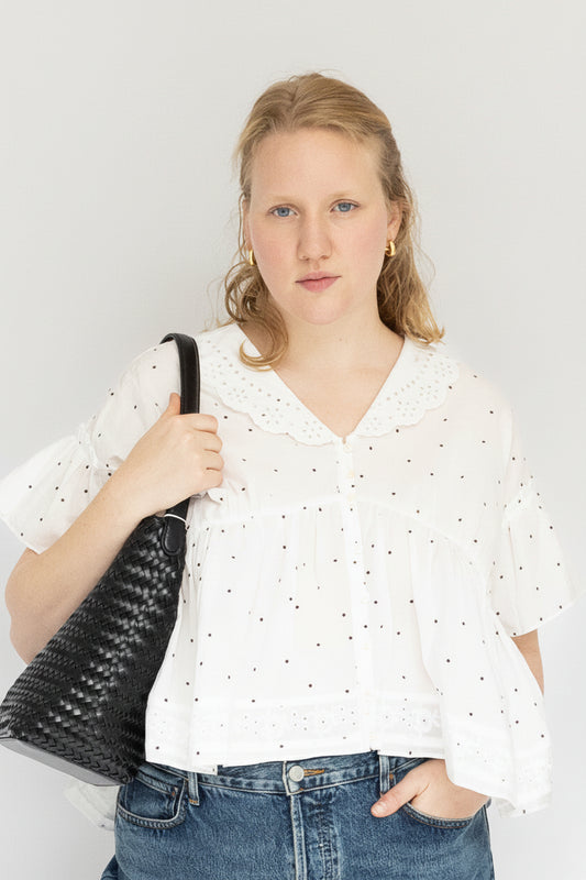 Woman wearing a white blouse and blue jeans holding a black handbag on a white background